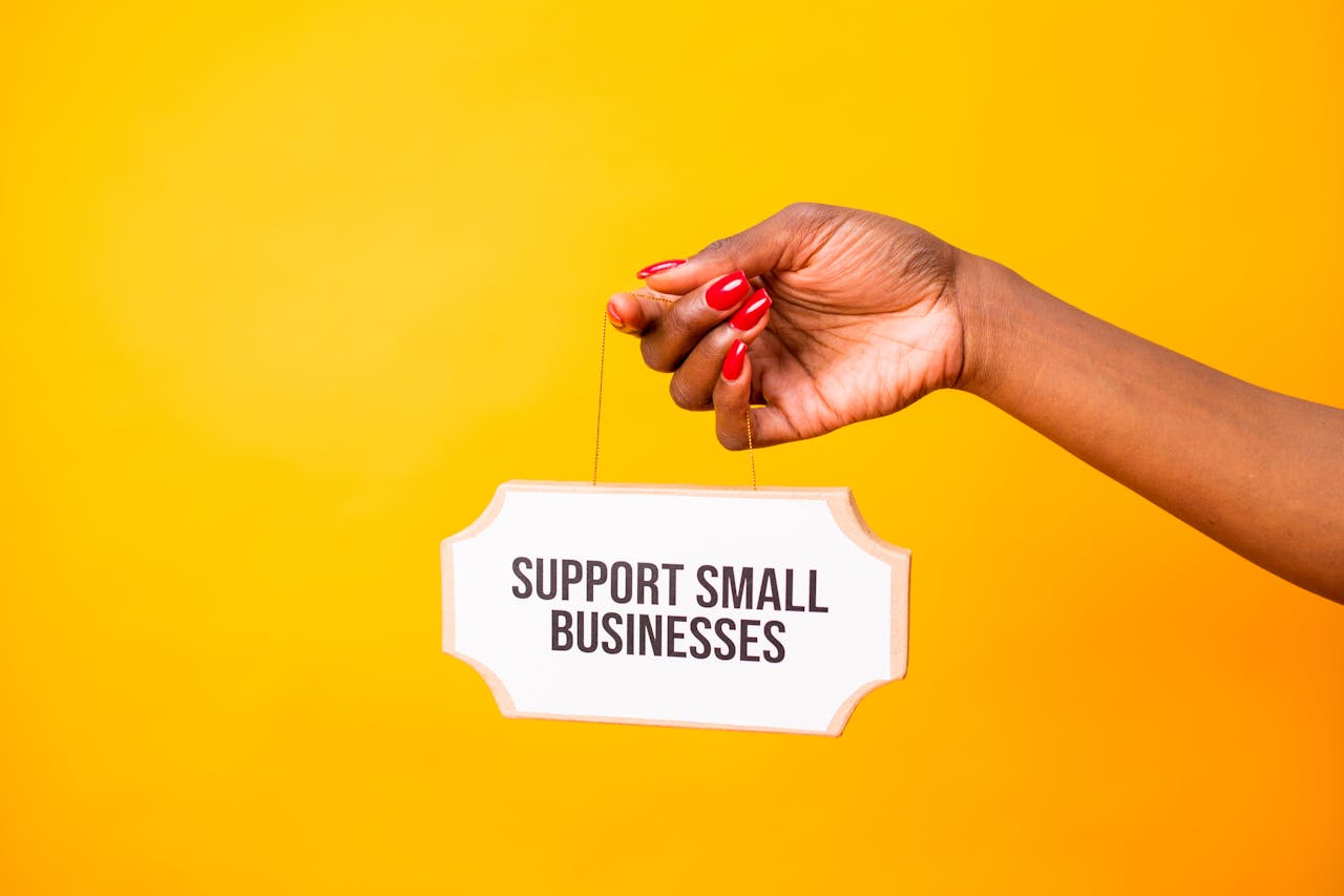 who-we-are Hand holding a 'Support Small Businesses' sign against a vibrant yellow background, promoting local commerce.